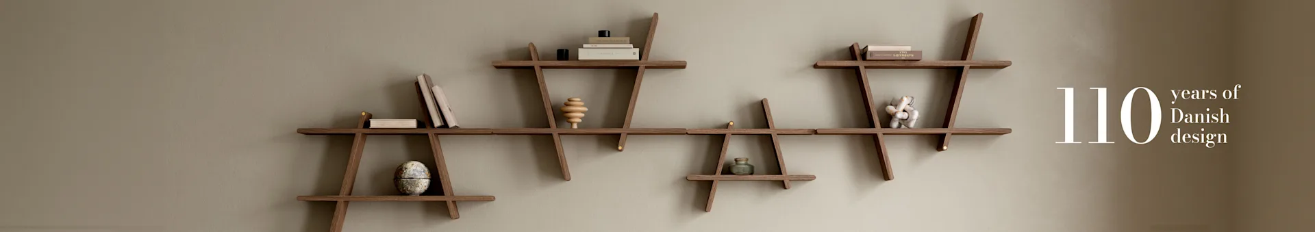 Modular wooden shelf system on a light brown wall, displaying books and decor. Text: '110 years of Danish design'.