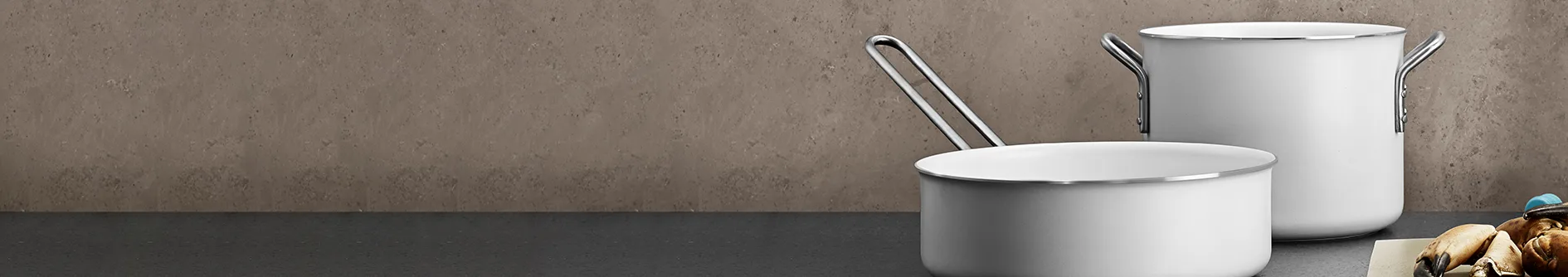 Two white cooking pots, one a saucepan and one a stockpot, on a dark countertop with a grey textured wall in the background.