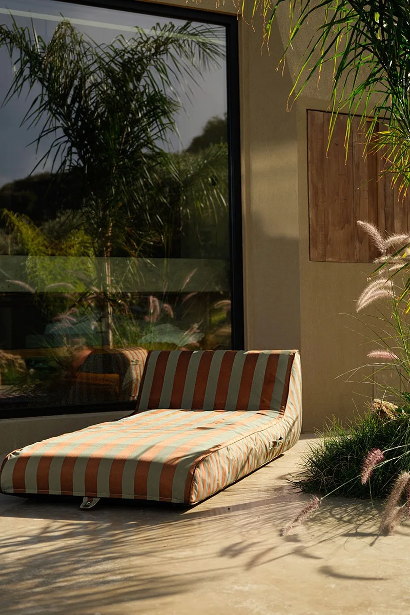Striped chaise lounge on a patio with a large window reflecting palm trees.