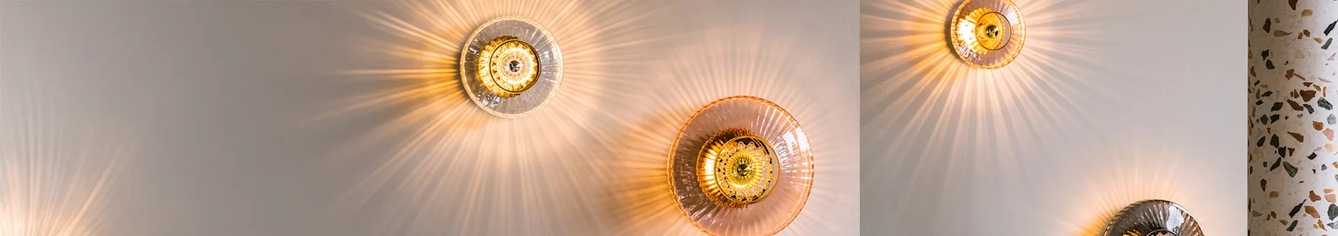 Three circular wall lights with ribbed glass shades casting radial light patterns on a light wall and a terrazzo column.