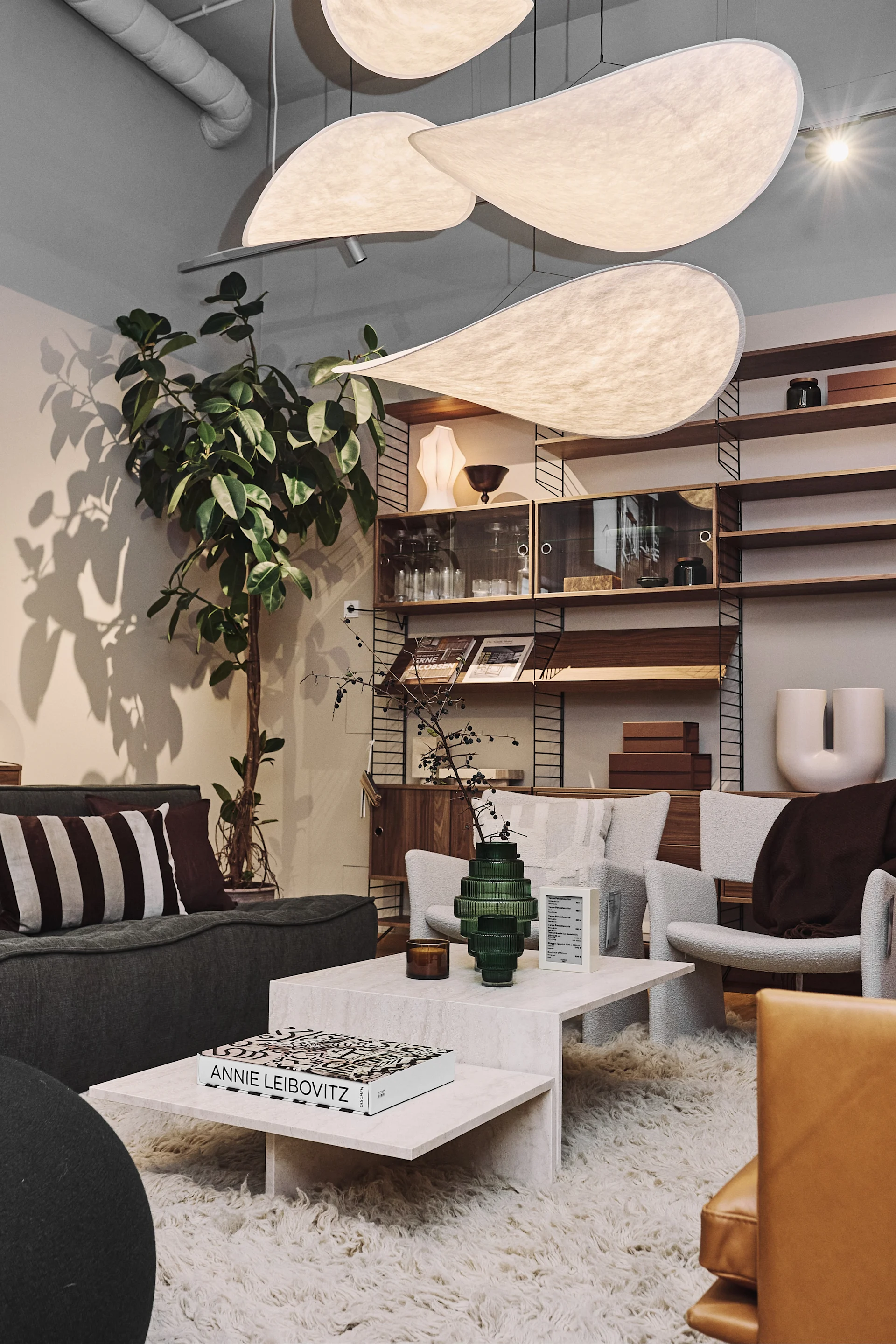 Interior with sculptural pendant lights, grey sofa, cream armchairs, coffee table, shaggy rug, and wooden shelves.