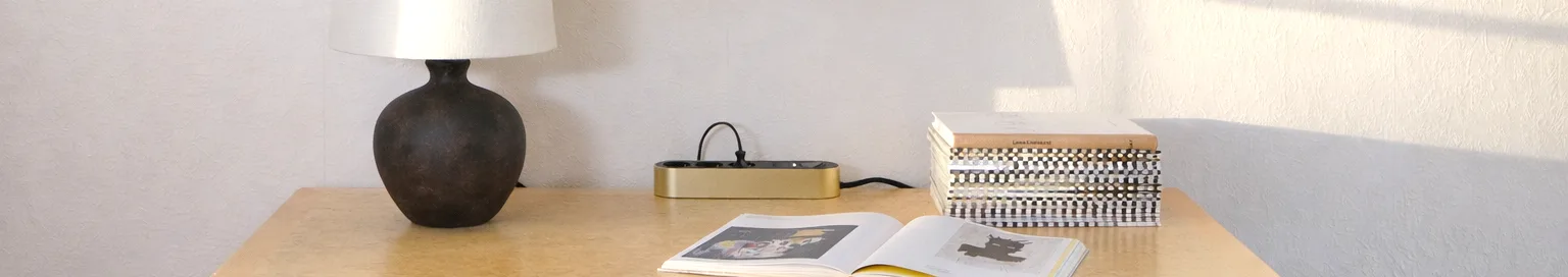 Gold power strip with three black outlets and a power button on a light surface.