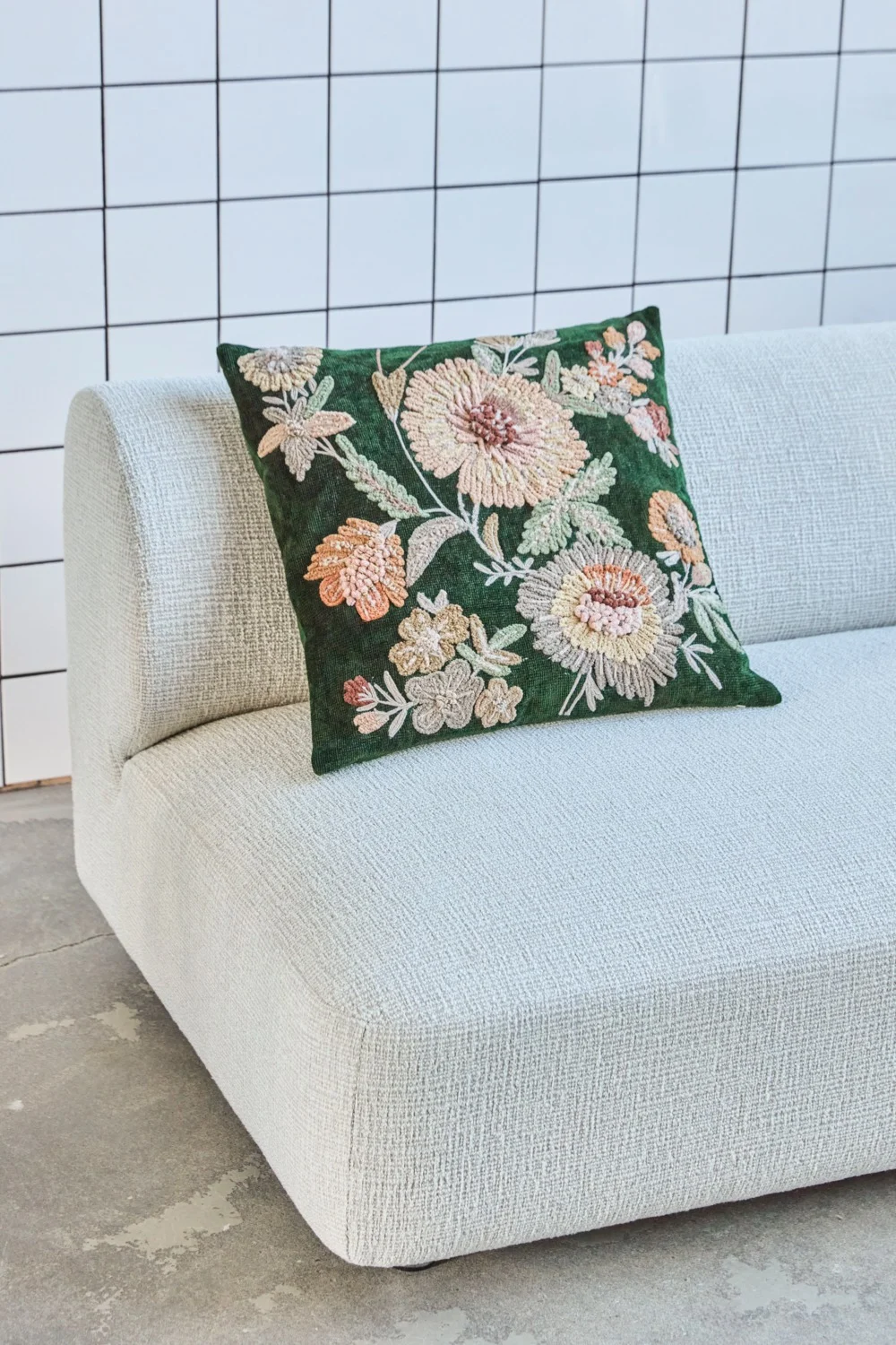 Dark green embroidered floral pillow on a light beige textured sofa.
