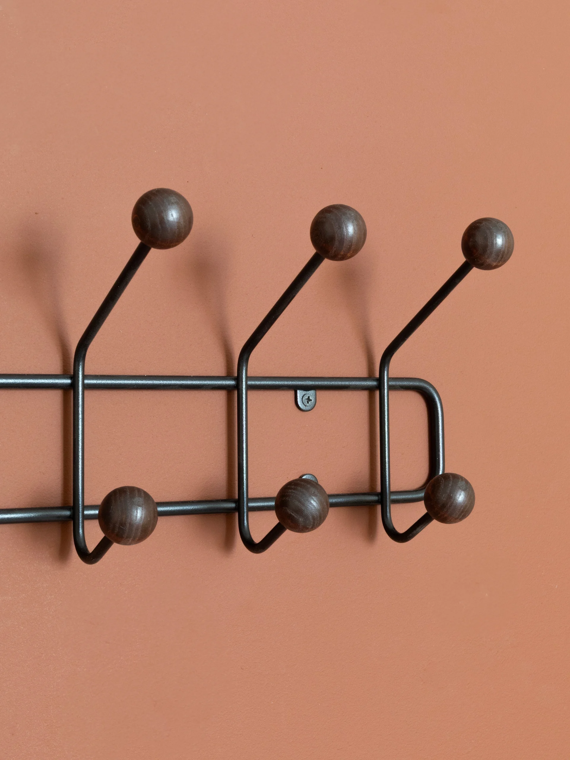A dark metal coat rack with six wooden ball-tipped hooks mounted on a reddish-brown wall.