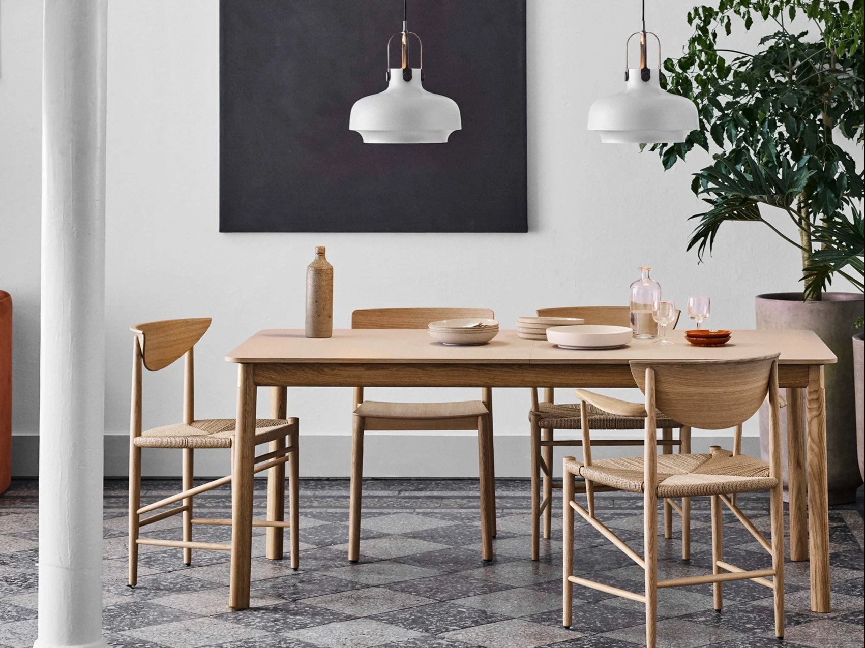 Modern dining room with a light wood table, woven chairs, white pendant lights, and a potted plant.