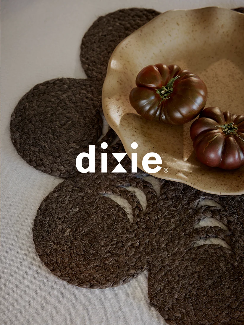 Two dark tomatoes in a beige bowl on dark braided placemats arranged like a flower, with the Dixie logo.