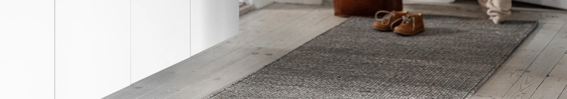 Light brown shoes on a gray runner rug on a light wooden floor.