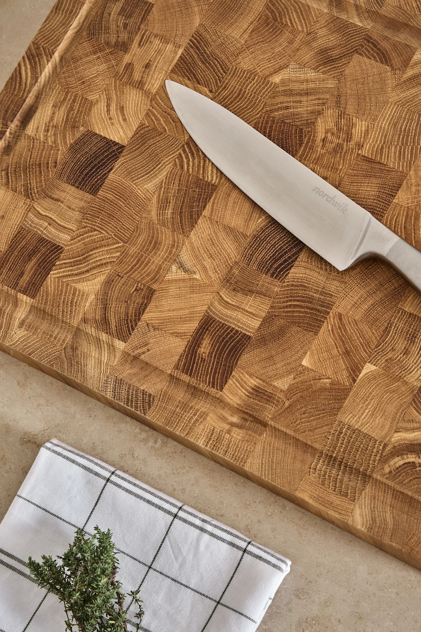 Nordwik chef's knife on a wooden end-grain cutting board with a checkered towel and fresh thyme.