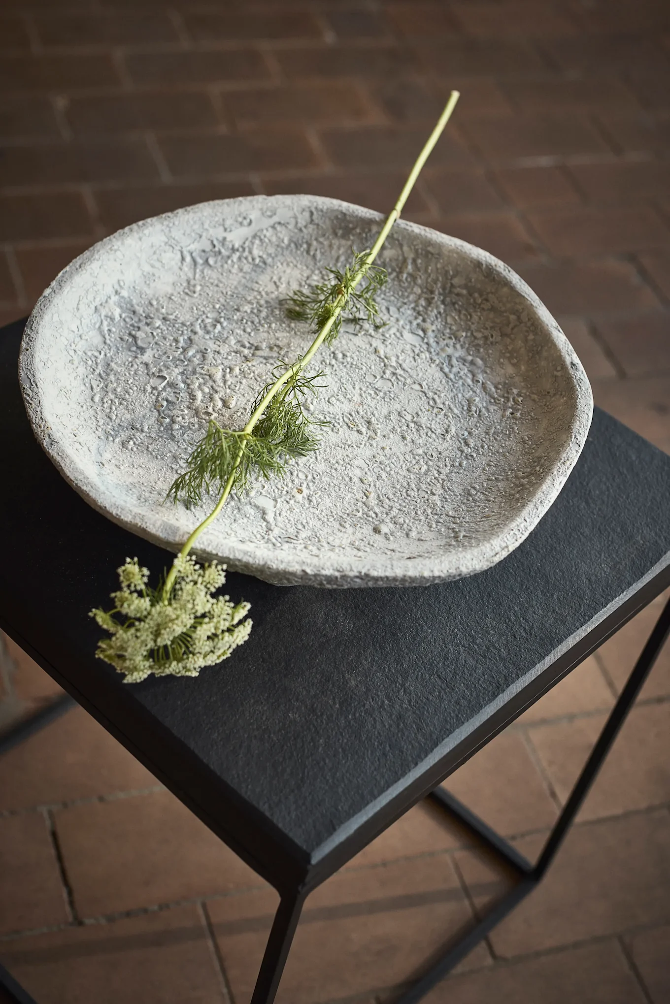 Textured gray bowl on a black table with a green stem and small white flowers.