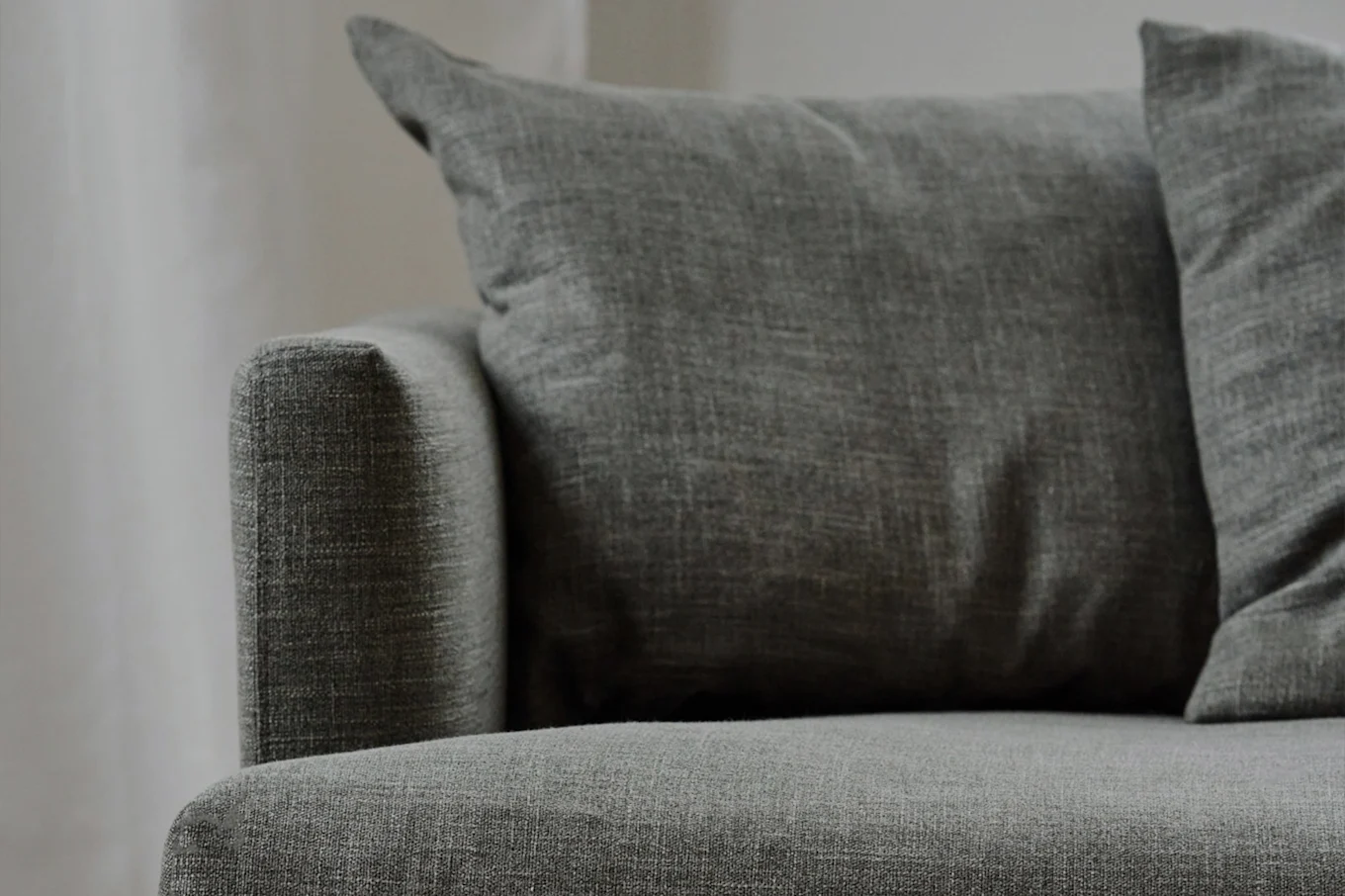 Close-up of a gray fabric sofa with textured pillows, showing the armrest and seat.