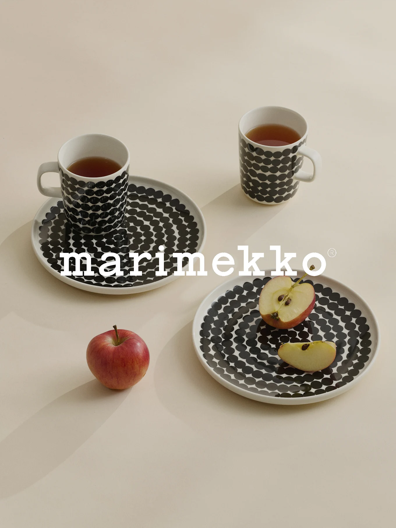 Two mugs and plates with black polka dots, tea, red apple, Marimekko logo.