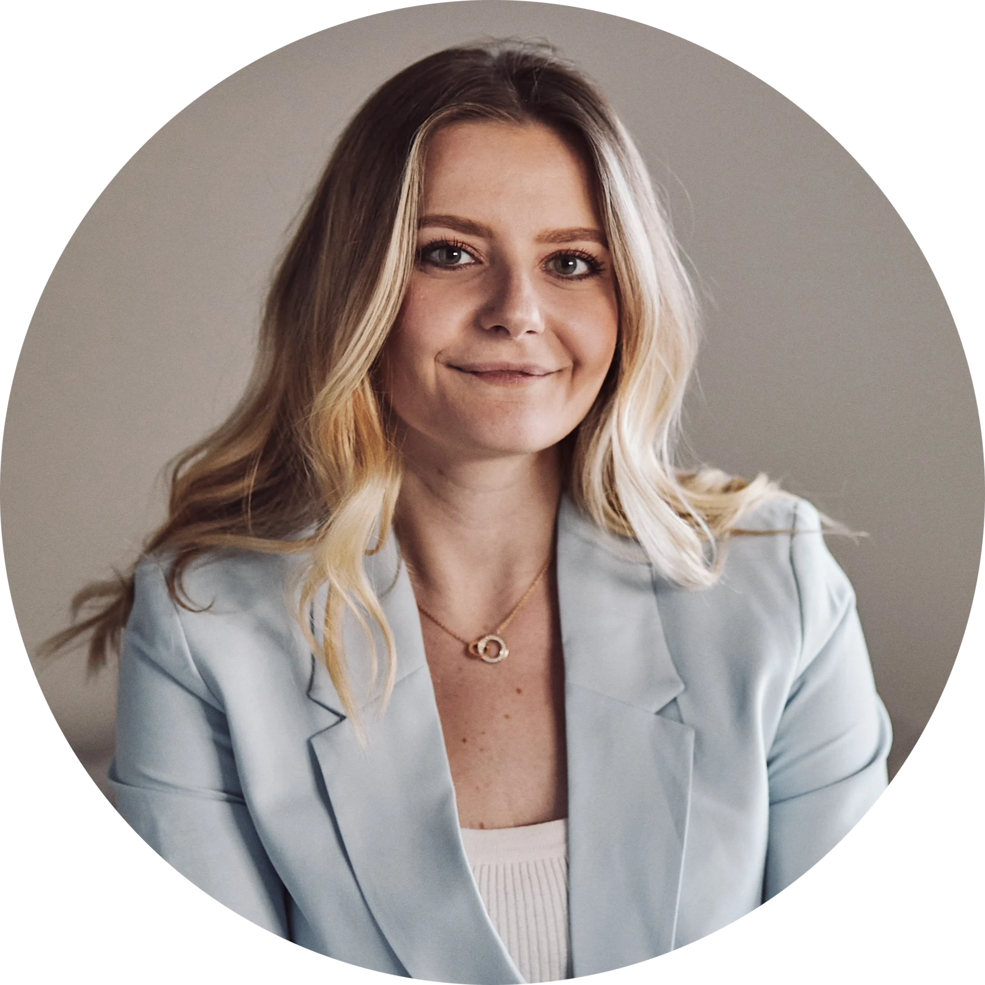 Smiling woman with long blonde hair, light blue blazer, and gold linked necklace. Circular portrait.