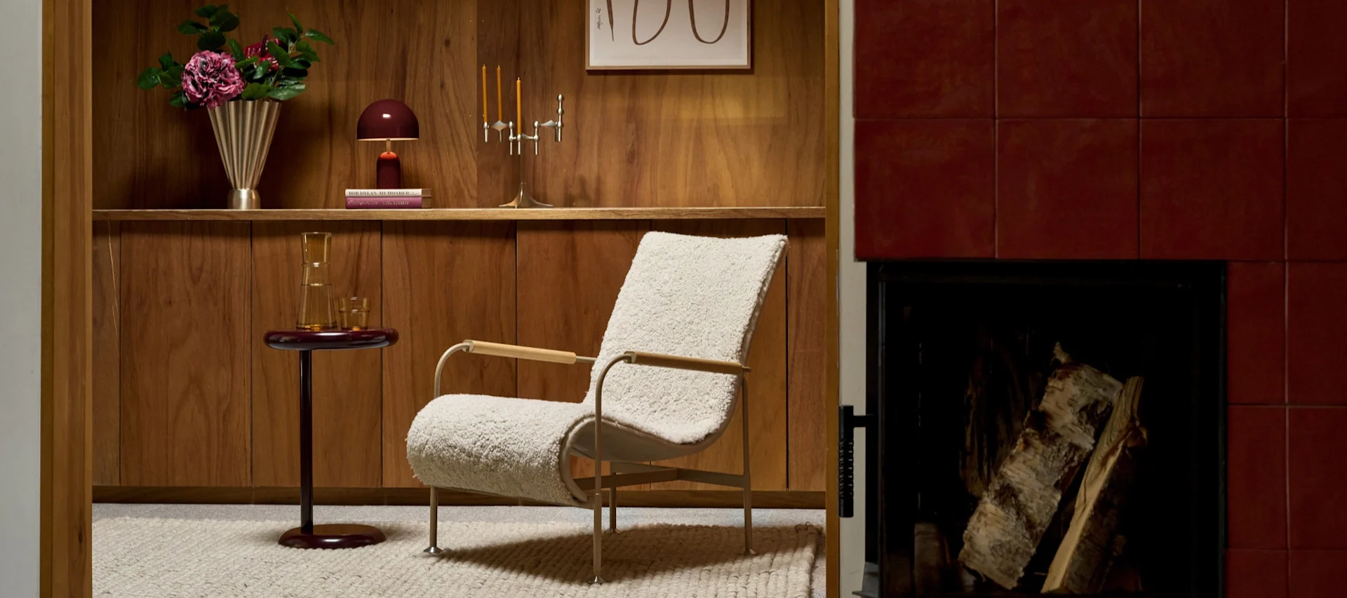 A split image of two interior scenes. Left: a blue and white striped table lamp on a wooden shelf. Right: a living room with a furry armchair, a side table, shelf with decor, and a fireplace.