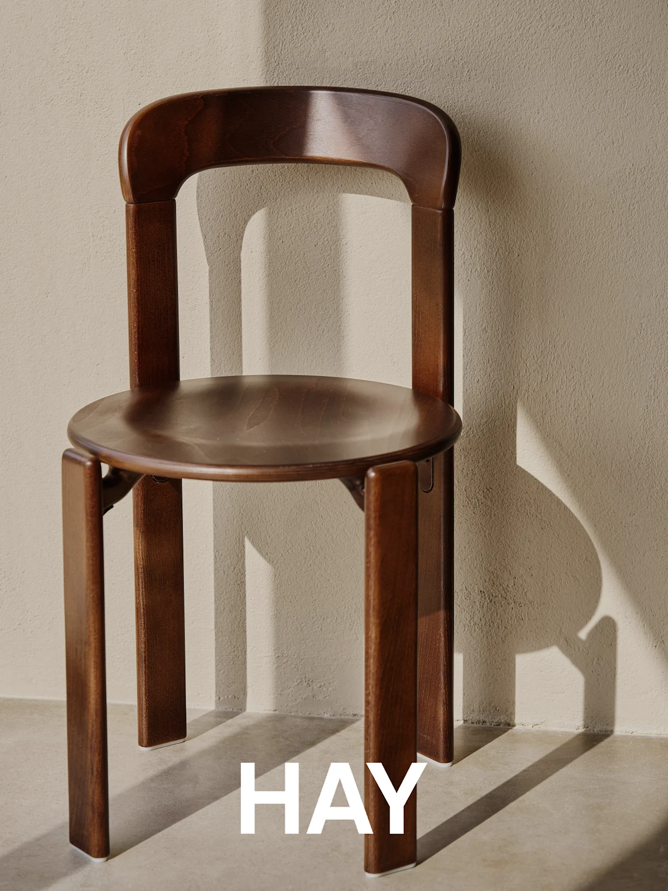 A dark brown wooden chair with a simple, modern design stands against a textured beige wall, with shadows.