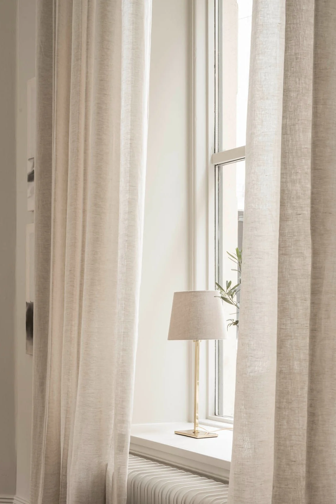 Light-colored sheer curtains frame a window with a brass table lamp on the sill.
