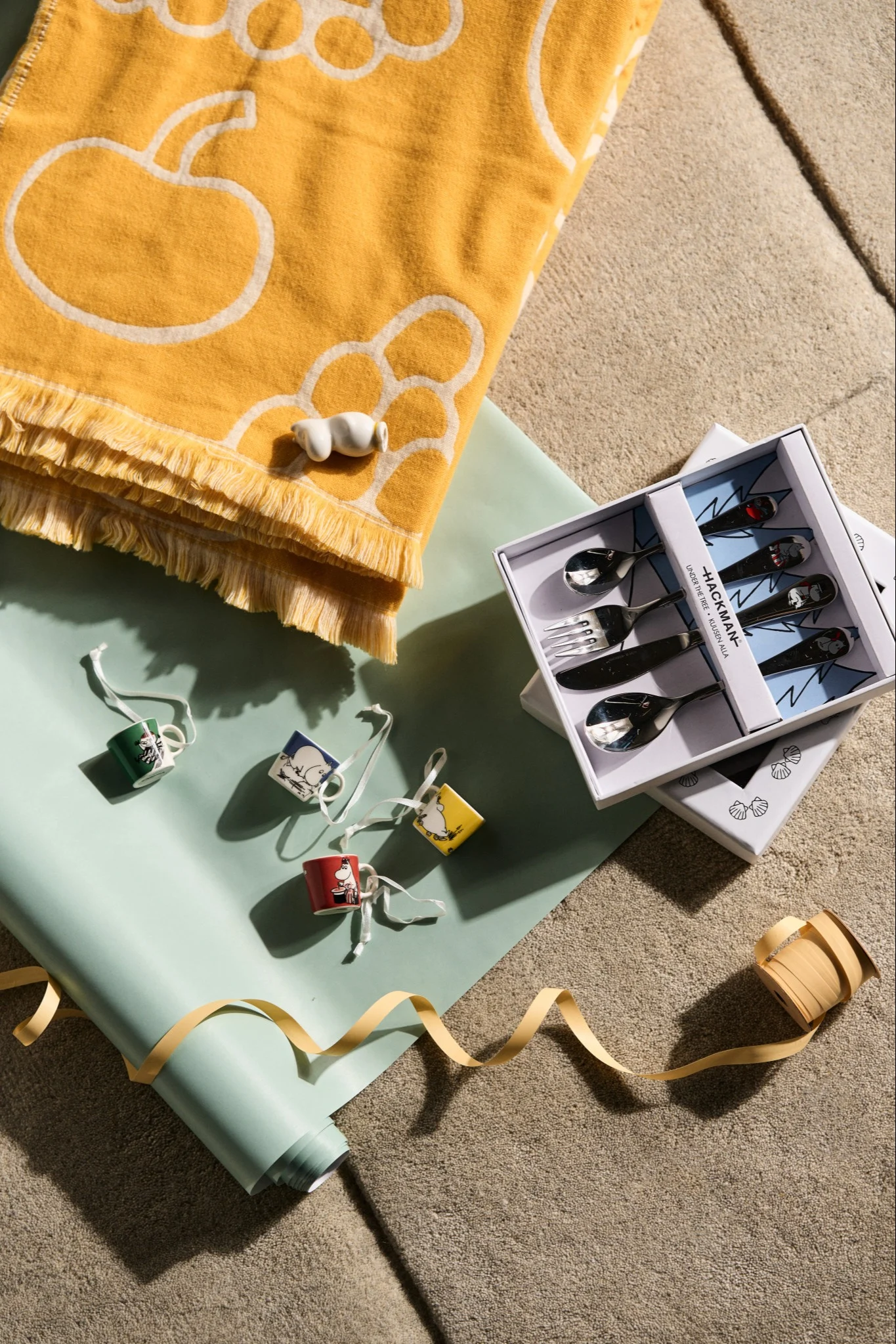 Creative gift ideas for a baby shower, here you see a collection of possible baby shower gifts. There are mini mugs, moomin figurines, a yellow blanket and a set of children's cutlery.