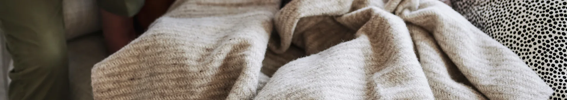 A close-up of various fabrics: smooth olive green, soft beige knitted, and a patterned fabric with small black polka dots.