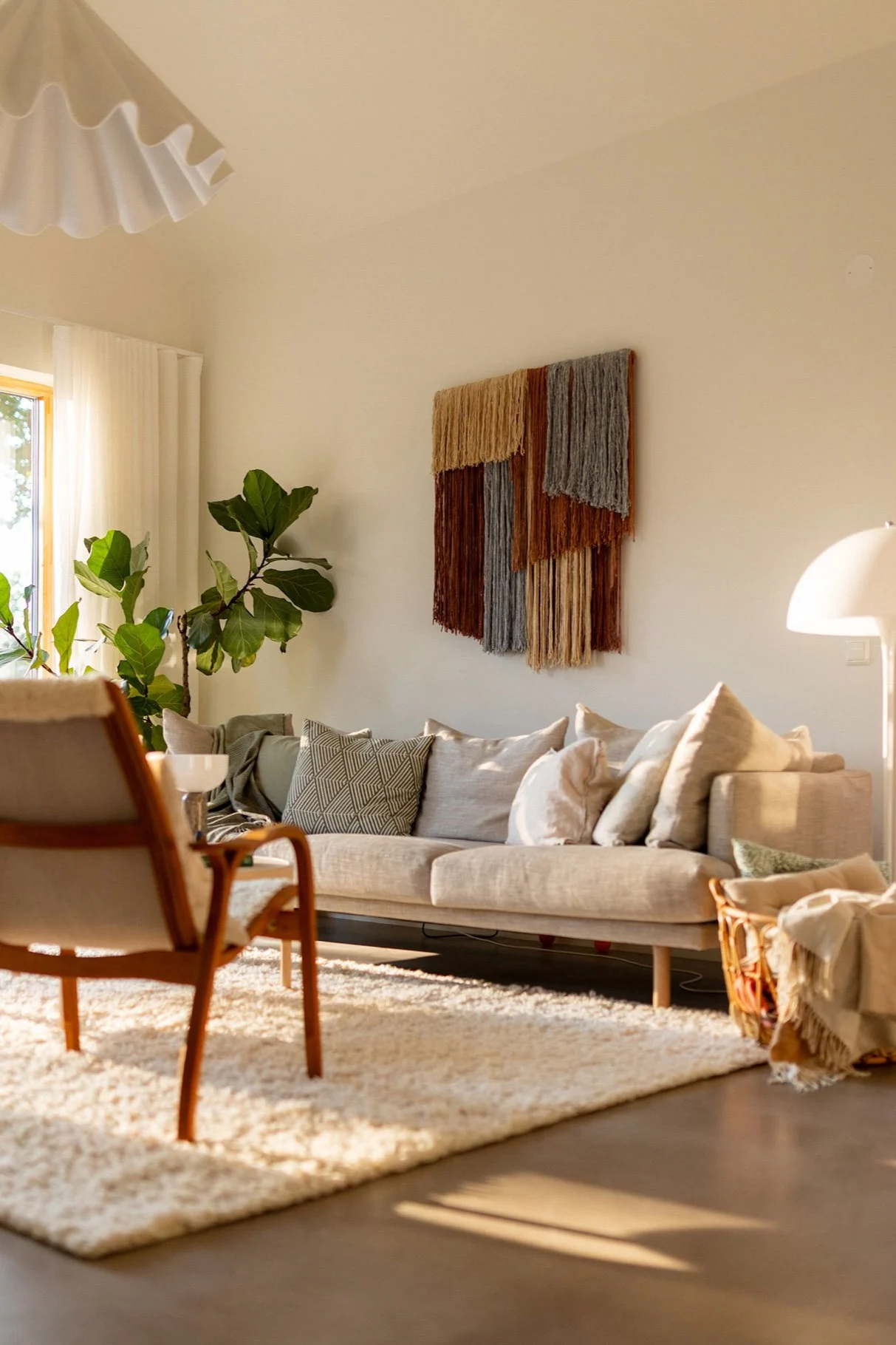 Sunlit living room with beige sofa, woven wall art, fiddle leaf fig plant, and fluffy rug.