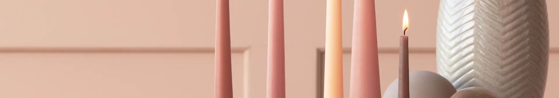 Several pastel-colored candles, one lit, next to a white chevron-patterned vase.