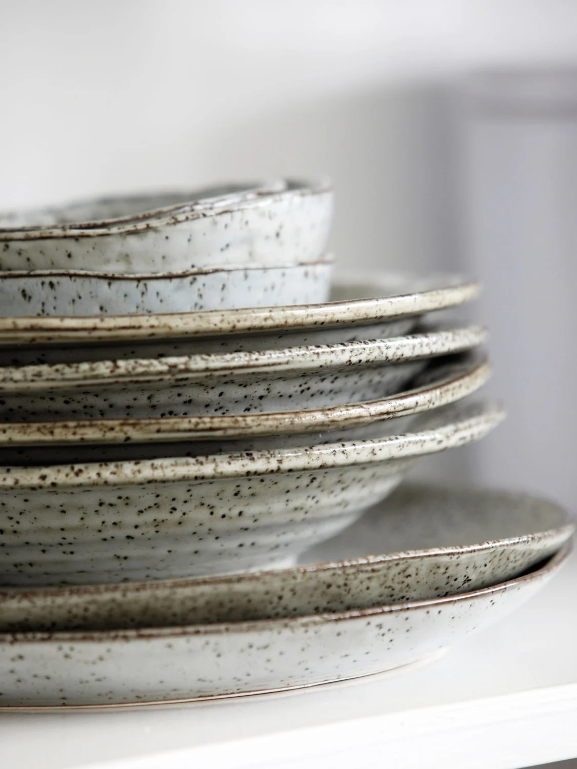 Stack of rustic speckled ceramic plates and bowls.