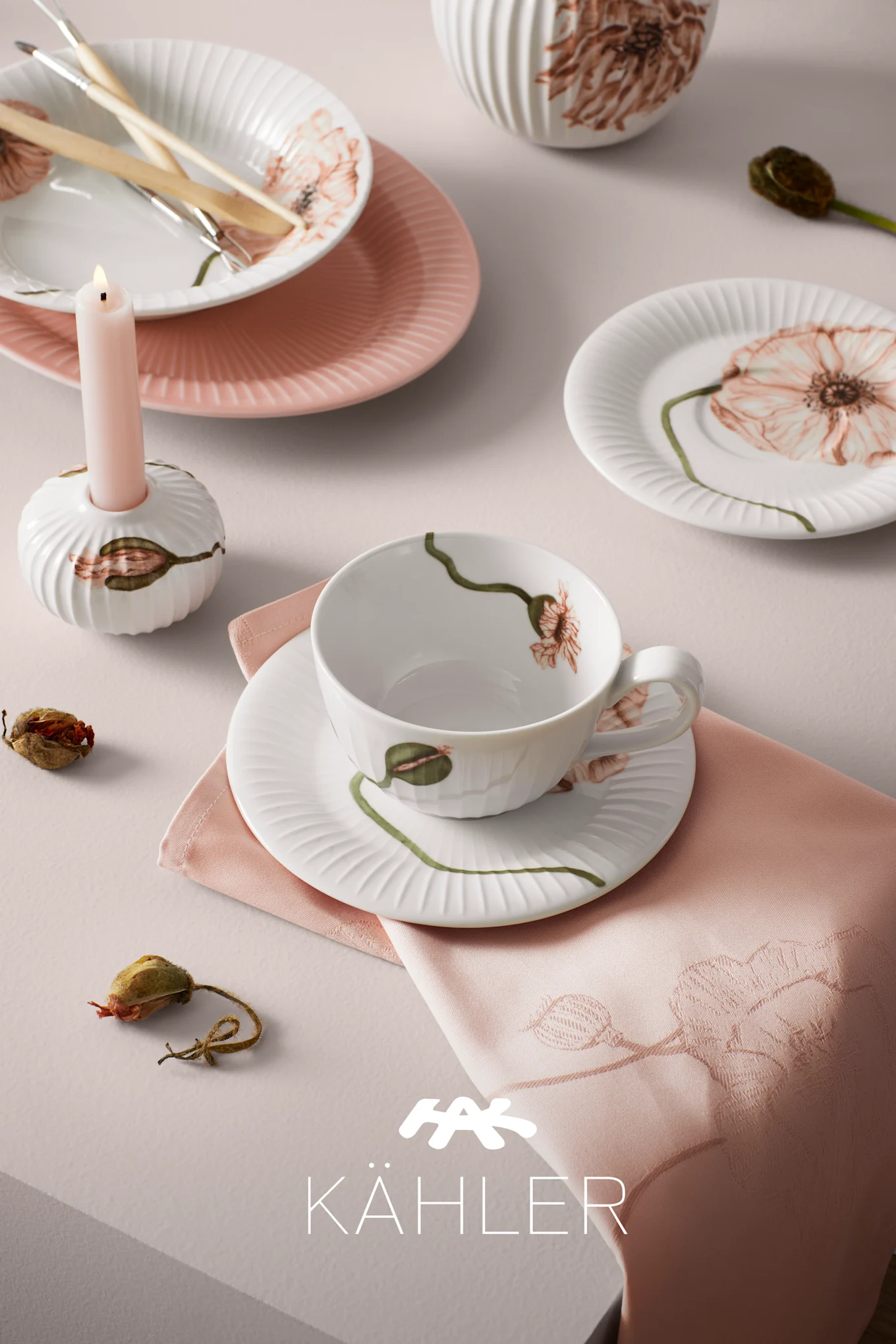 White and pink fluted dishes, cup, saucer, and candle holder with poppy designs, along with a pink napkin.
