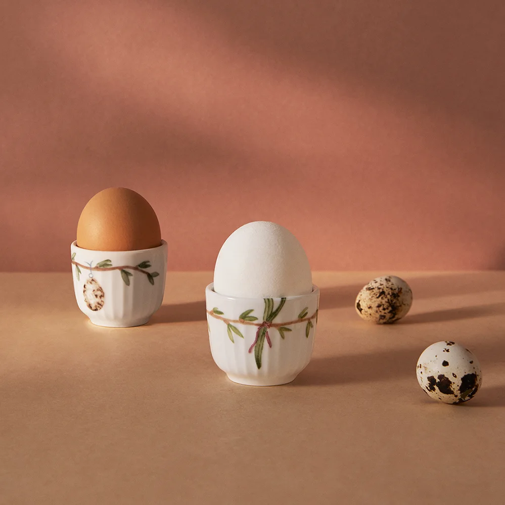 Two decorative egg cups, one with a brown egg and one with a white egg, alongside two speckled quail eggs.