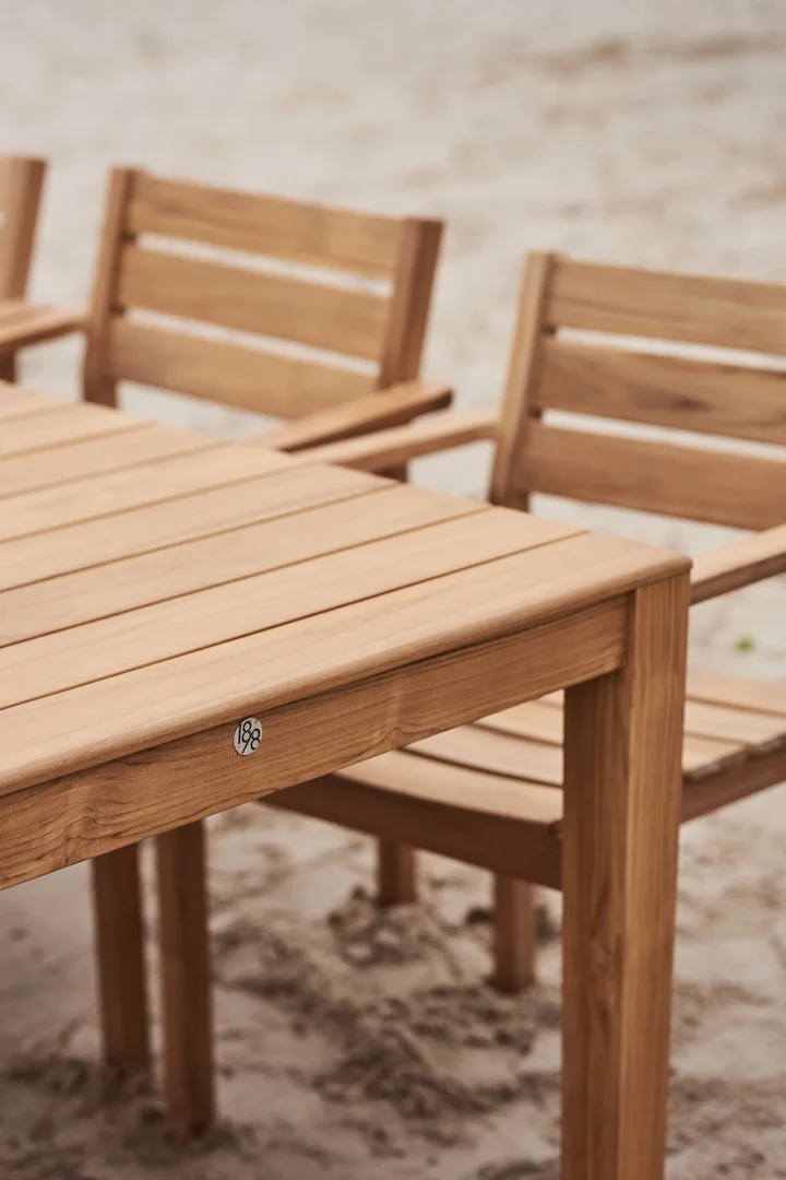 Wooden outdoor dining table with chairs on sand, featuring a '188' plaque.