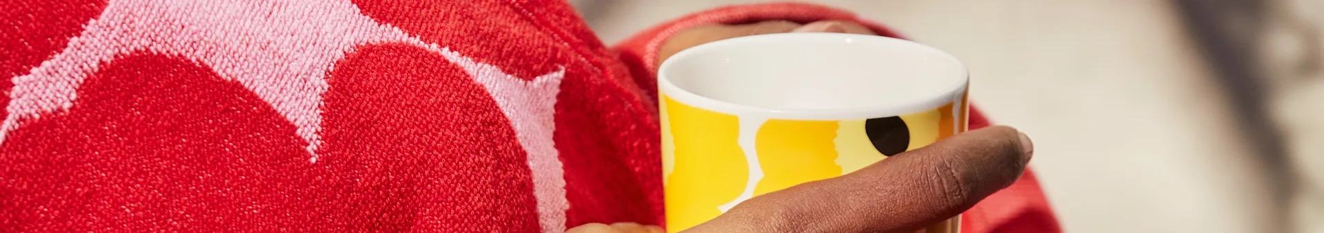 Person holding a yellow mug with abstract design, wrapped in a red patterned towel.