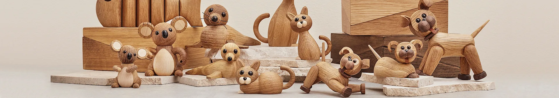 A playful arrangement of wooden animal figurines: koalas, a seal, a cat, and a dog, displayed on light stone blocks.