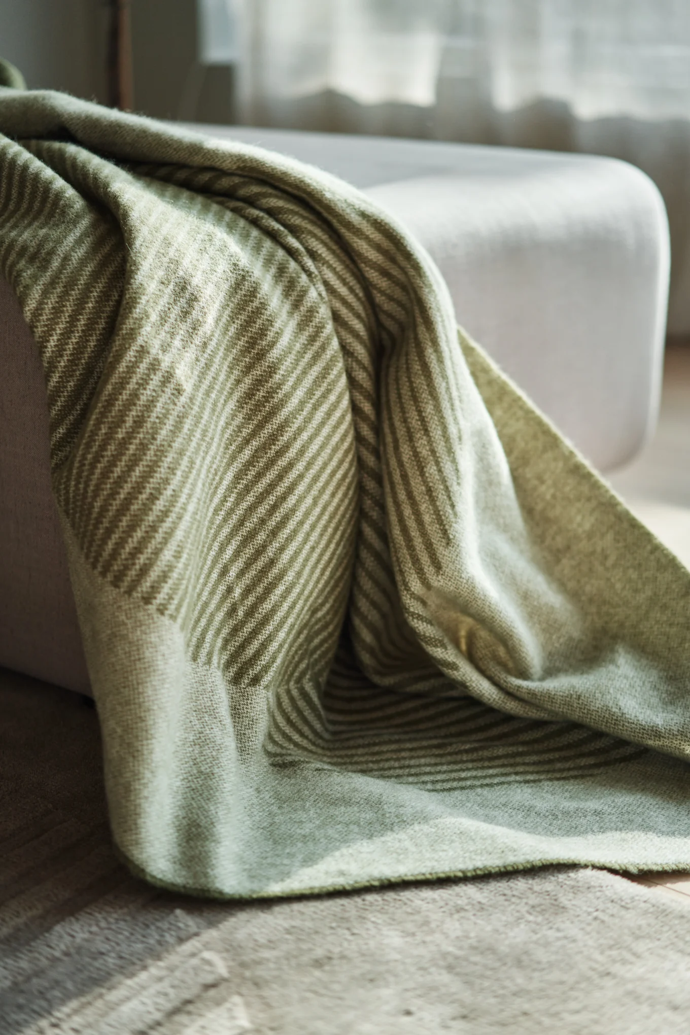 A soft, light green blanket with diagonal stripes draped over a light gray ottoman in natural light.