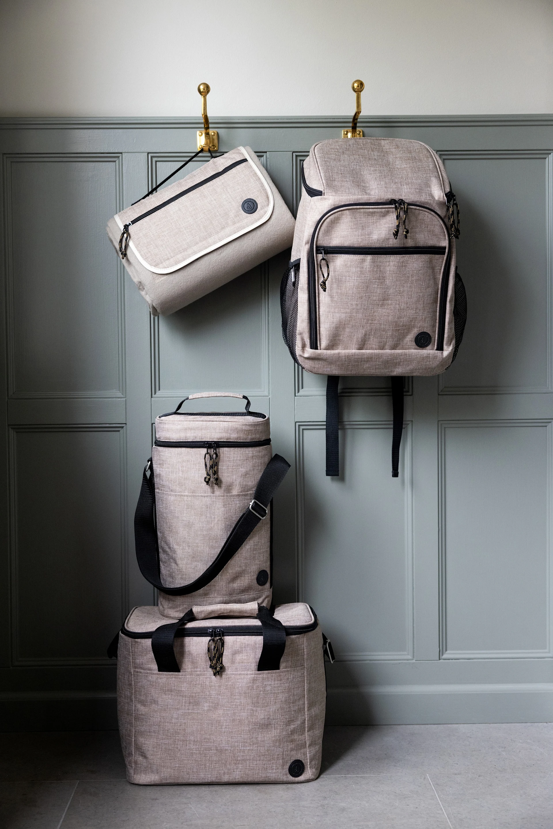 Four light beige bags: a flat bag and a backpack hang on hooks, a cylindrical cooler and rectangular cooler stack below.