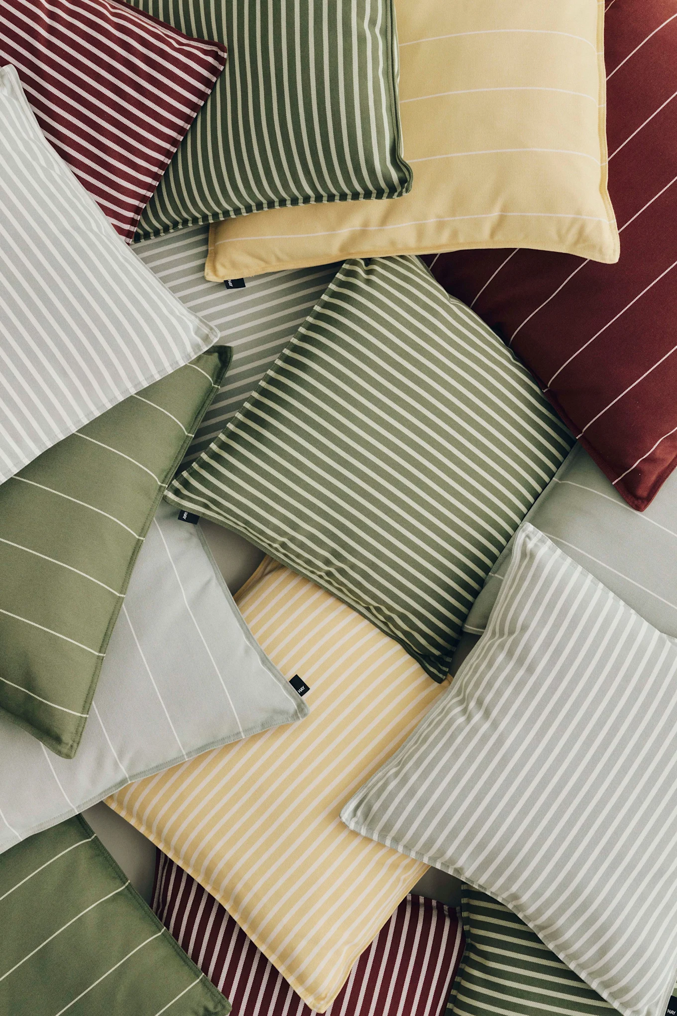 A pile of striped throw pillows in red, yellow, light green, and light gray, with stripes in various orientations.