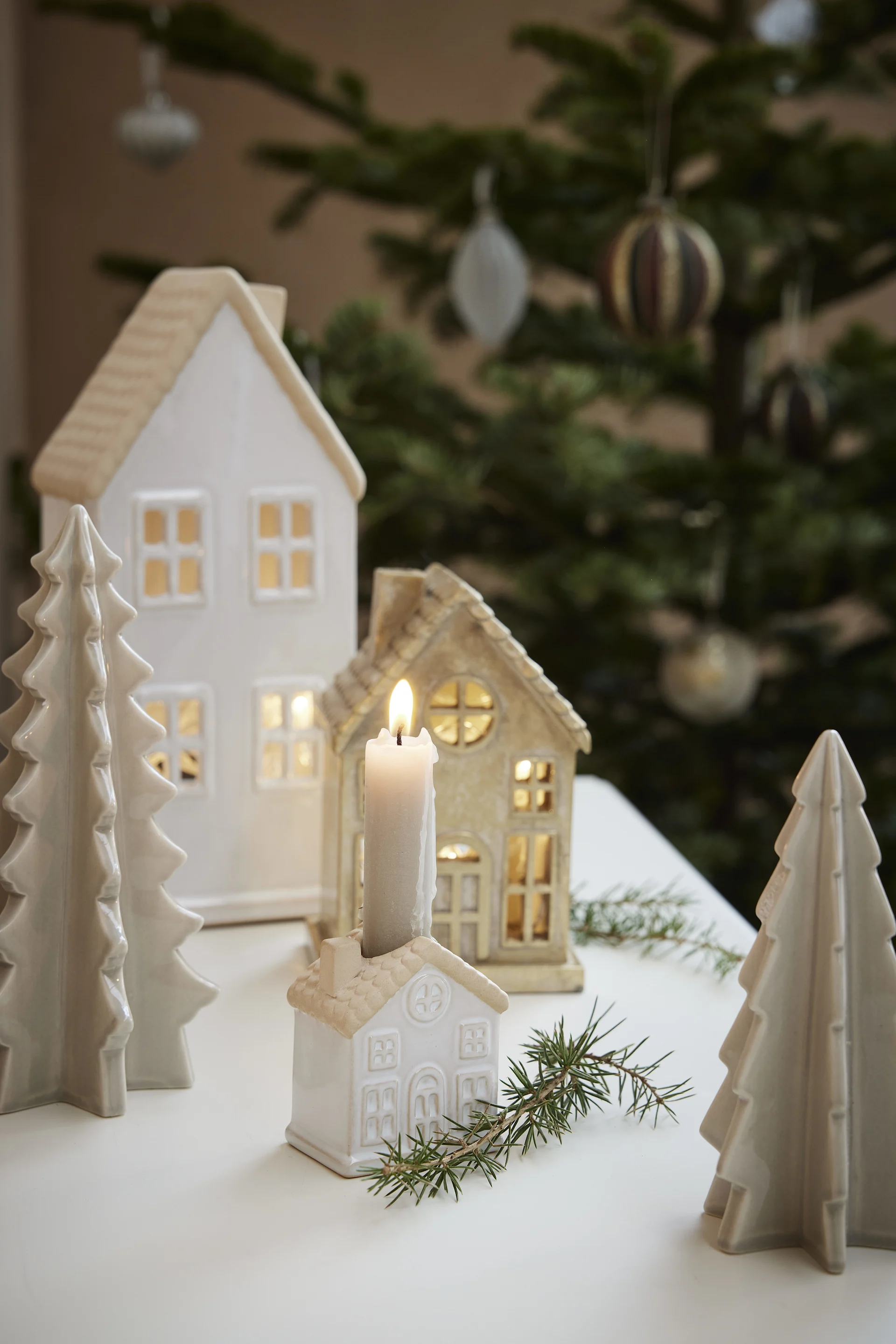 Christmas scene with illuminated ceramic houses, decorative trees, and a lit candle.