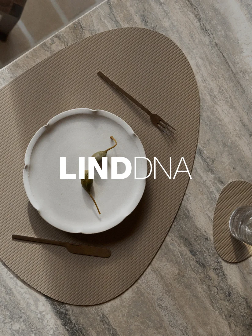 A dining table set with a ridged taupe placemat, white plate with capers, and bronze cutlery.