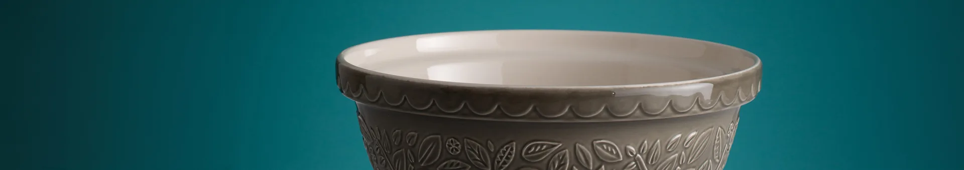 Close-up of a gray ceramic planter with a light beige rim and an embossed leaf pattern on a teal background.