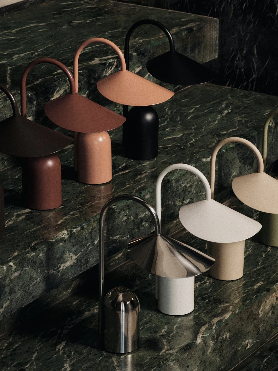 A collection of modern table lamps in various colors and finishes, arranged on green marble steps.