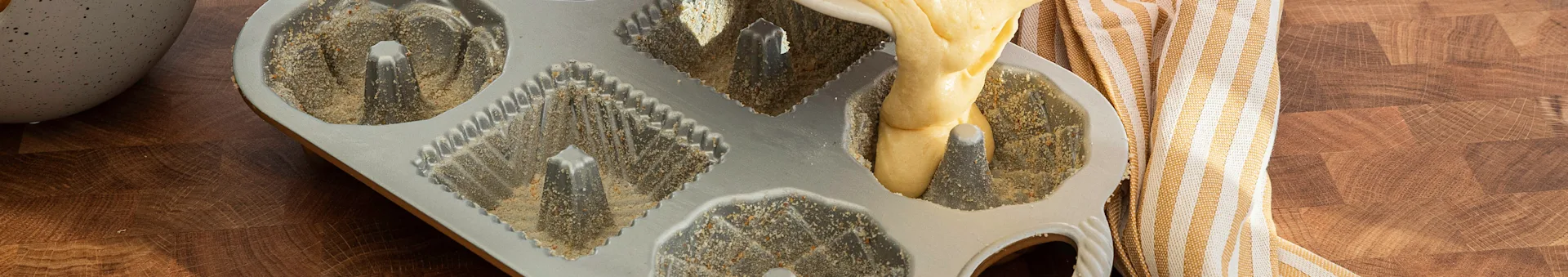 Batter is poured into a greased and floured bundt cake pan on a wooden surface.