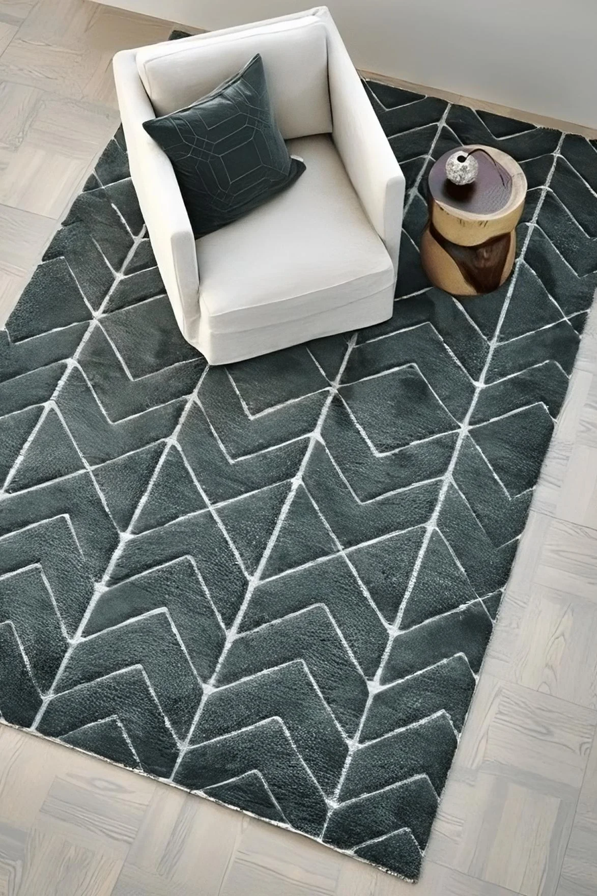 Overhead view of a living room corner with a cream armchair, green geometric pillow, and a unique wood side table on a dark green rug with white zigzag patterns.