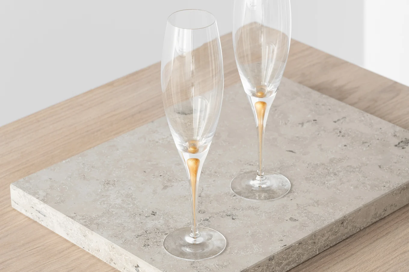 Two clear champagne flutes with gold teardrop stems on a stone slab.