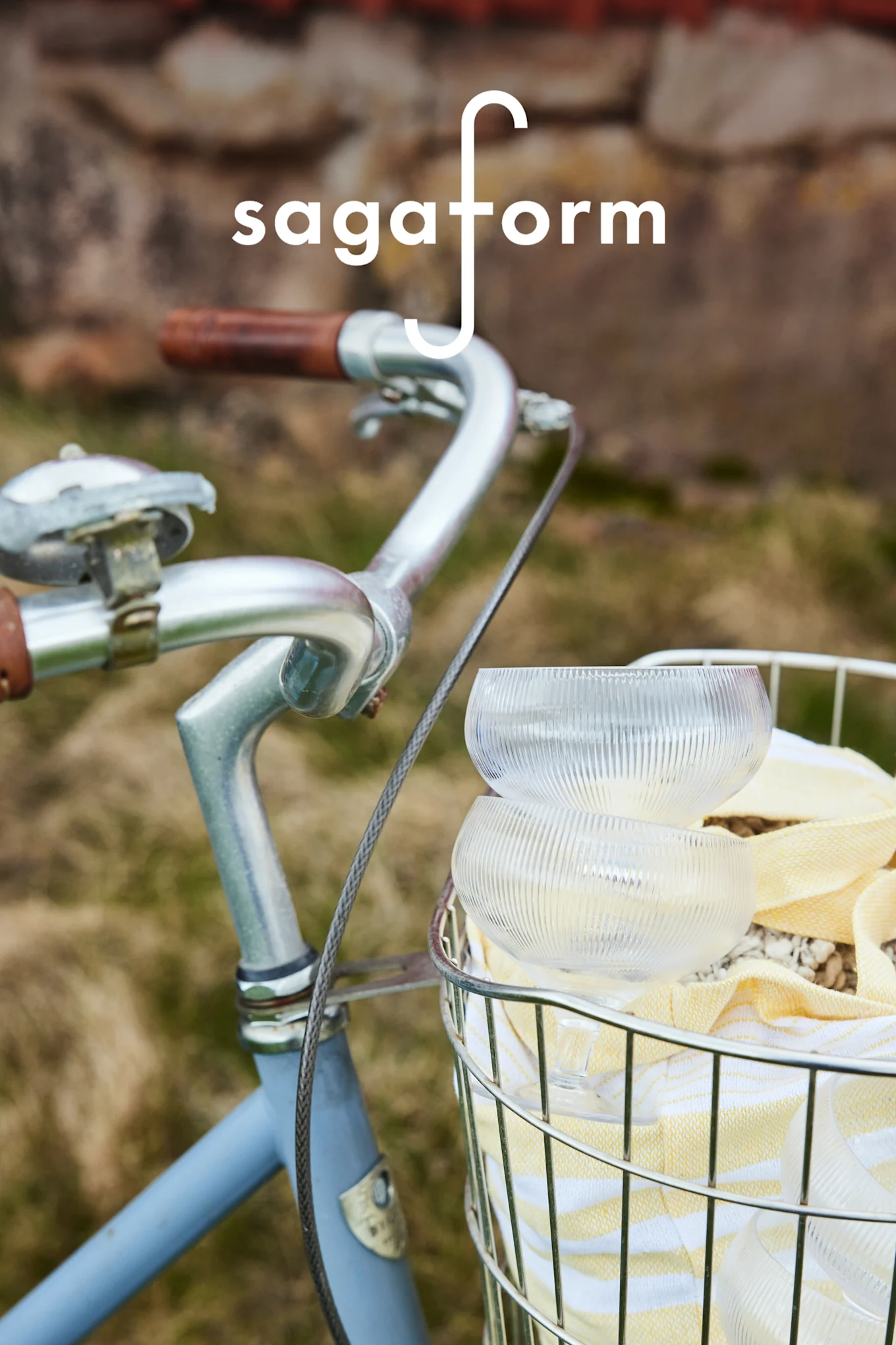 Two clear, ribbed glass bowls and a yellow striped towel in a bicycle basket. 'sagaform' logo.