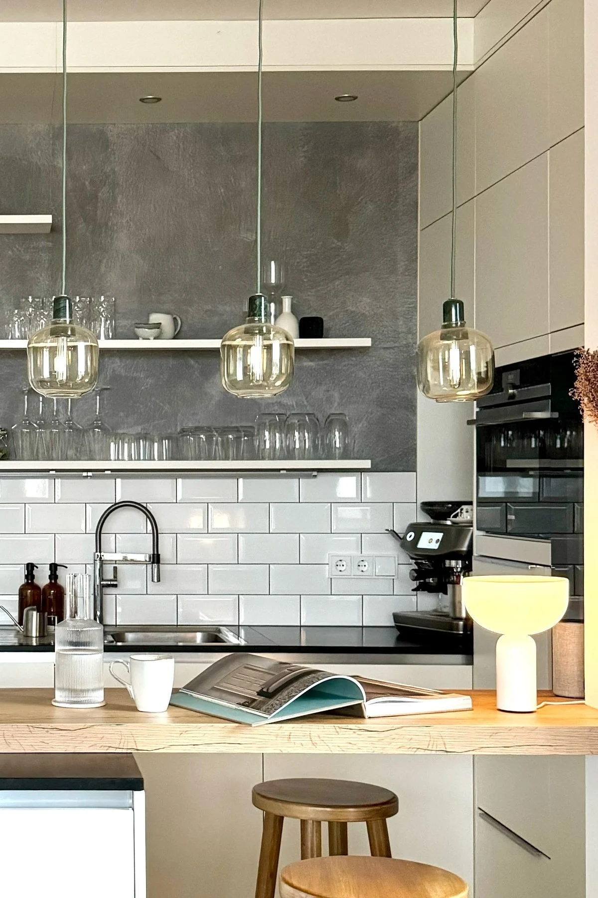 Modern kitchen with wooden counter, white subway tiles, amber pendant lights, and a book on the bar.