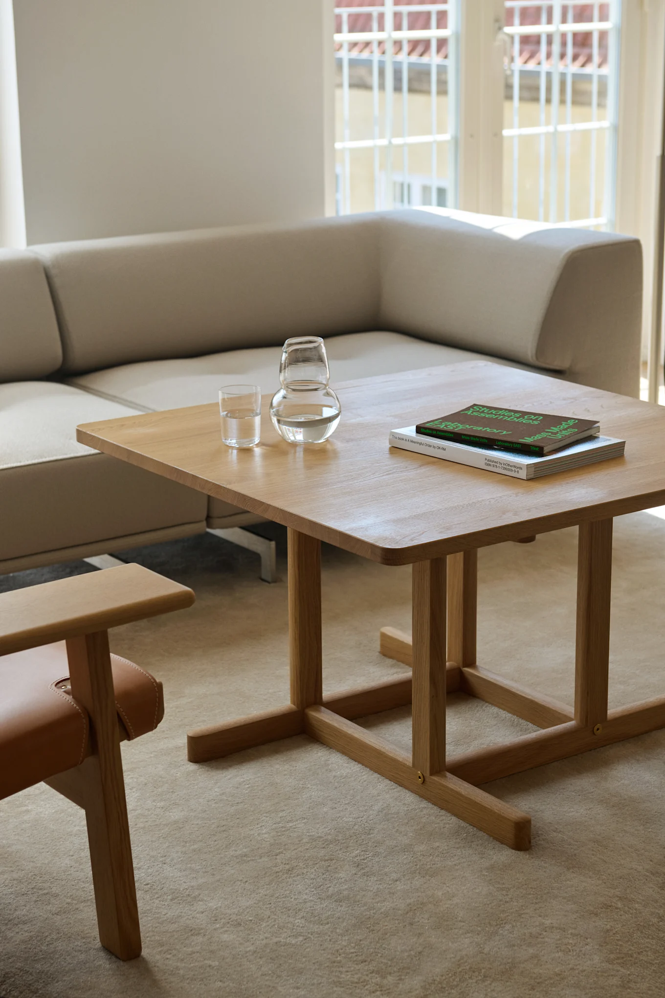A light wooden coffee table with two glasses of water and books, in front of a light sofa and next to a chair.