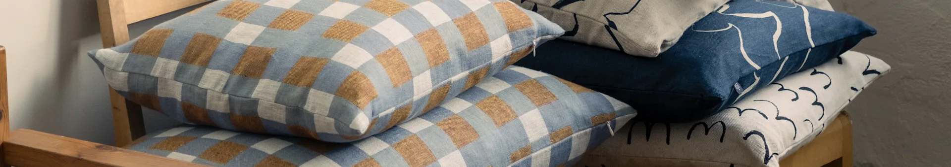 Stacked pillows on a wooden chair, featuring checkered blue and brown, and abstract patterned blue and beige designs.
