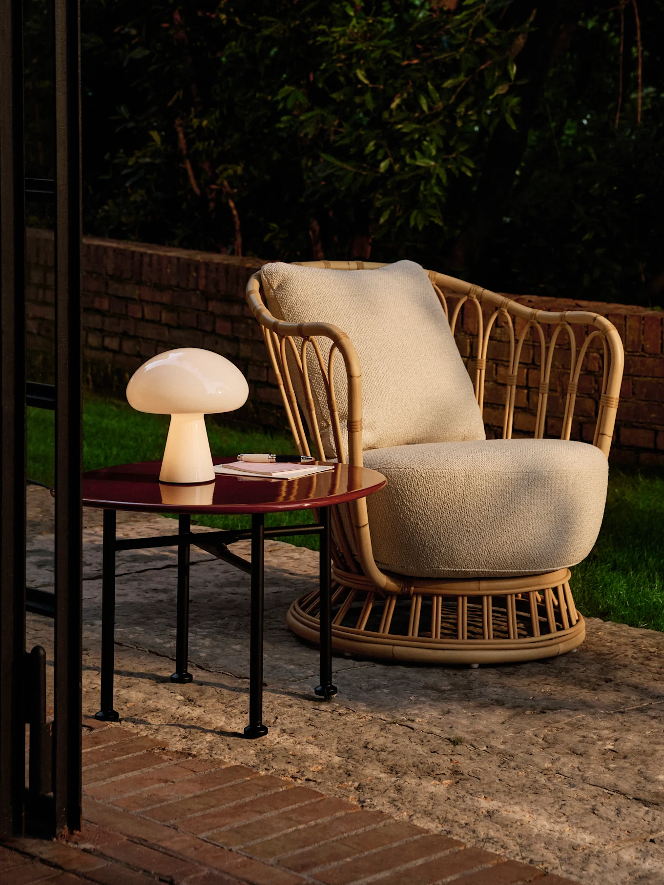 Mushroom lamp on a red side table next to a rattan armchair on a patio at dusk.
