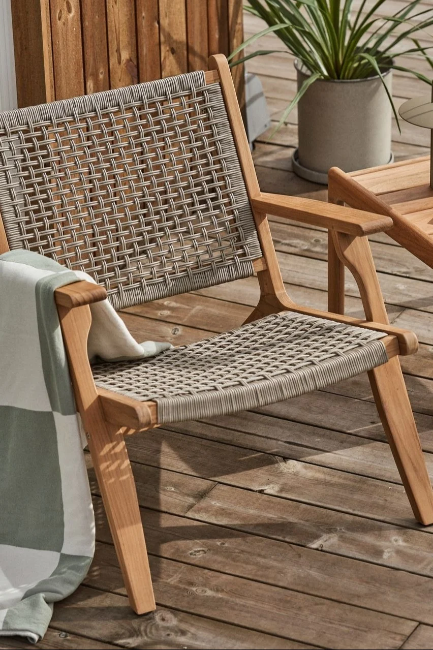 Outdoor wooden chair with woven gray straps and a striped blanket on a wooden deck.
