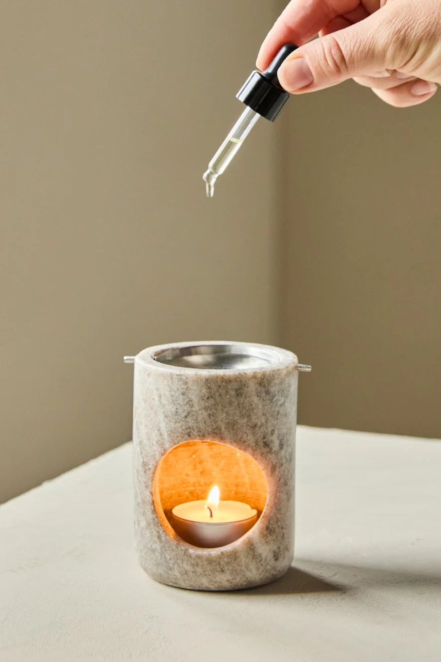 Hand dripping essential oil into a lit stone diffuser.
