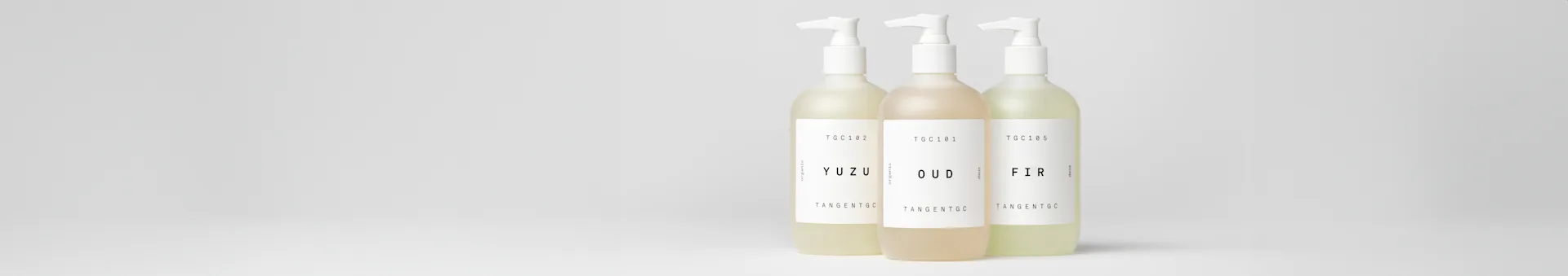 Three frosted pump bottles of soap in light yellow (Yuzu), amber (Oud), and light green (Fir) on a white background.