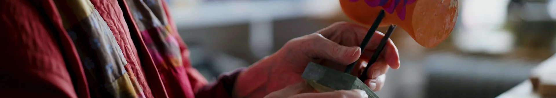 Close-up: hands decorating an orange object with purple details.