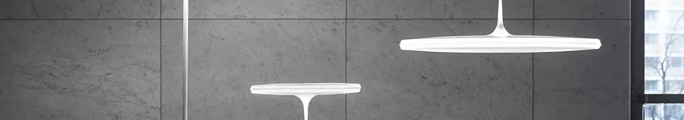 Two modern white disc-shaped pendant lights against a gray tiled wall.