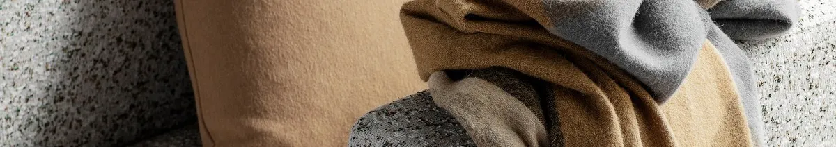 Close-up of a beige pillow and a striped throw blanket with grey, brown, and beige colors on a speckled surface.